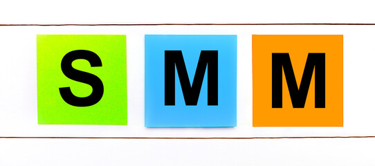 On a white wooden background there are three colorful bright stickers with text SMM Social Media Marketing
