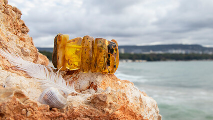 Yellow Baltic amber bracelet on the rock against the sea. Shiny handmade natural amber jewelry.