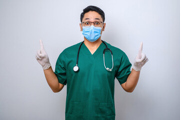 Surprised or curious male nurse in green scrubs, medical mask, pointing fingers up, inform patients how prevent corona infection