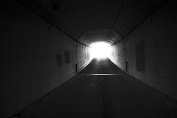 a black and white corridor with a white light at the end. an underground tunnel in black and white. the light of paradise at the end of a dark corridor