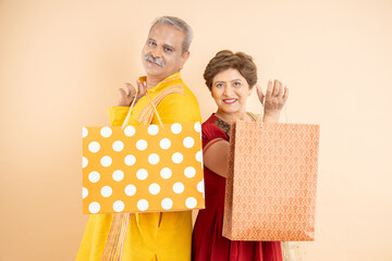 Happy mature indian couple wearing traditional cloths holding shopping bags and gift boxes, celebration diwali festival together isolated on plane studio background. Senior husband wife.