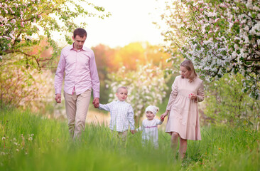 Happy parents mom and dad, daughter and son, young family outdoors in spring against the backdrop of blooming apple and cherry trees