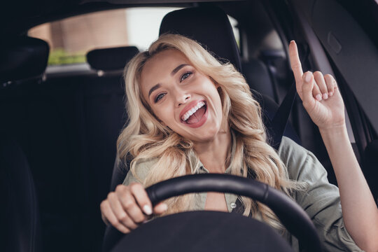 Photo of cheerful overjoyed person sitting driver seat hold wheel point finger enjoy radio station