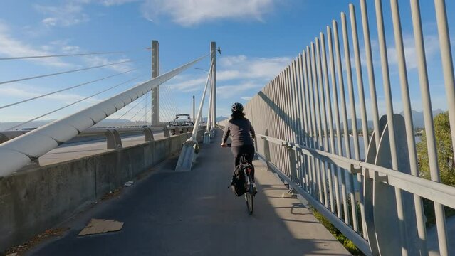 Woman Bike riding on a Bicycle Path over Golden Ears Bridge over the Fraser River. Pitt Meadows, Langley, Greater Vancouver, British Columbia, Canada. High quality 4k footage