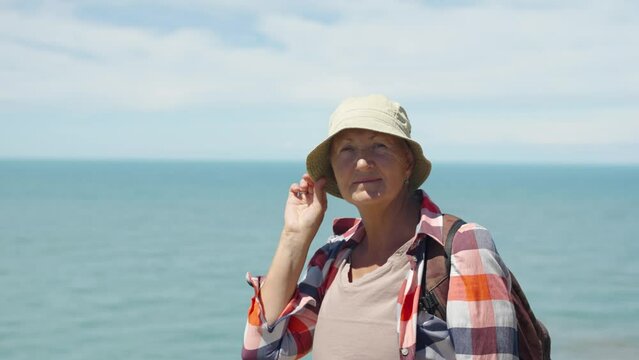 Portrait of an adult female tourist in a hat against the background of the sea and blue sky