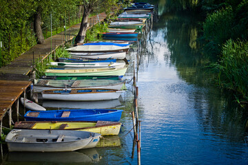 Fototapeta na wymiar small colorful boats moored in a row at the pier in the river channel. in the background trees and plants