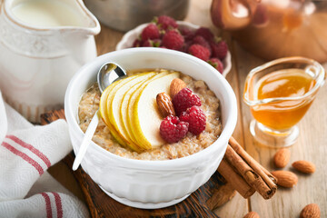 Oatmeal. Bowl of oatmeal porridge with raspberry, pear and honey on old wooden table background. Hot and healthy food for Breakfast, top view, flat lay