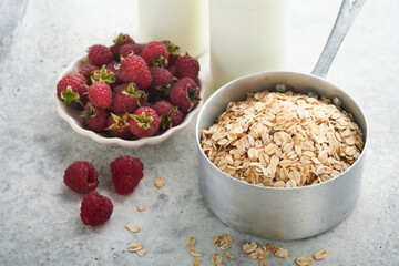 Ingredients for cooking oatmeal or granola with oats, milk, raspberries, honey and almonds on gray concrete old table background. Ingredients for healthy breakfast.