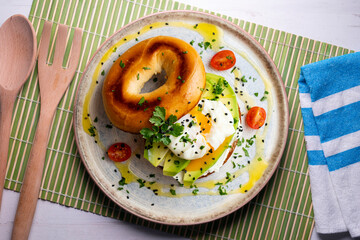 Toasted baggel with cream cheese, avocado, organic cherry tomatoes and poached egg. Vegan brunch.