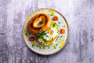 Toasted baggel with cream cheese, avocado, organic cherry tomatoes and poached egg. Vegan brunch.