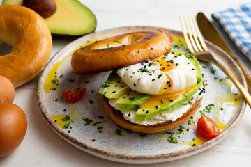 Toasted baggel with cream cheese, avocado, organic cherry tomatoes and poached egg. Vegan brunch.
