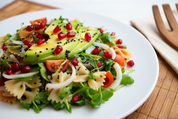 Argula salad with pasta bows, avocado, cherry tomatoes, pomegranate and sesame.