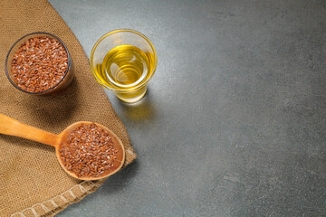 Flax seeds in bowl and flaxseed oil in glass on gray stone textured background, close-up, selective focus. Linseed oil