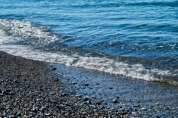 Sea blue wave with foam on pebble beach. Close-up of the coastline 