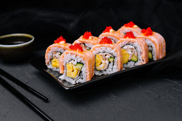 Sushi roll with fried salmon on black plate