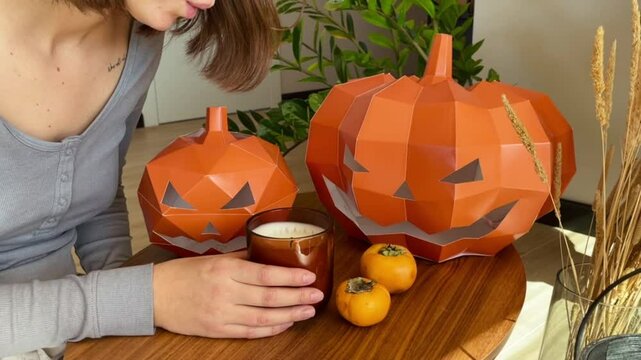 The girl blows out the candle on the holiday of Halloween in the living room. Around the head of pumpkin, candles and dried flowers