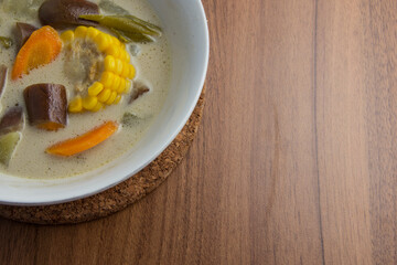 Sayur lodeh or vegetable gravy coconut milk is a traditional Indonesian culinary food from Java in a white bowl served on a brown wooden table.