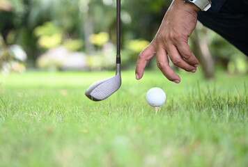 A golfer's hand is put a white golf ball on tee embroidered on a green lawn with a blur green golf course background. Right hands without gloves placing or remove the golf ball on a tee. 
