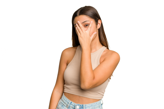 Young Indian woman isolated cutout removal background blink at the camera through fingers, embarrassed covering face.