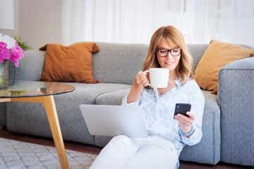 Middle aged woman test messaging and drinking tea while working from home
