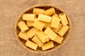 Several raw yellow cannelloni in a straw plate on a jute cloth, macro, top view.