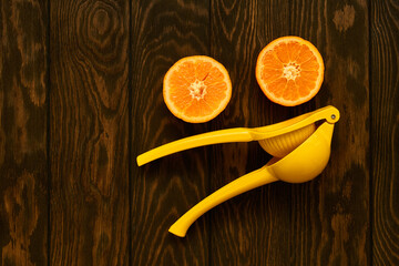 Stylish yellow hand juicer and mandarin halves on a dark wooden table close up