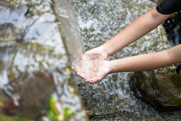 Closeup hands of a child girl are outstrecthed to receive the fresh water in nature that spill from the small dam in the stream