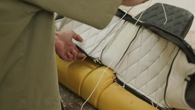 Cropped shot of unrecognizable worker sewing details to each other while making leather car seat cover at factory