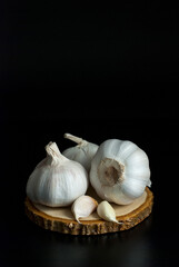 Garlic put on a wooden cutting board on a black floor.