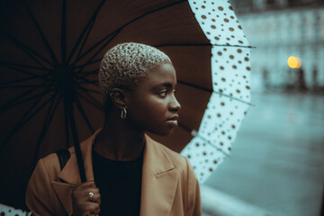 A low-key portrait of a pensive cute youthful black female with short hair painted in white,...