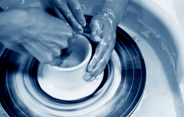 Potter teaching child to make ceramic pot on the pottery wheel