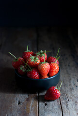 Strawberries are placed in a black ceramic cup and put on a rustic wooden floor.