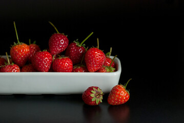 Several strawberries are housed in white ceramic vessels and placed on a black floor.
