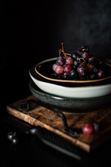 Red grapes in a retro plate on a dark background. Rustic atmosphere. Creative idea.