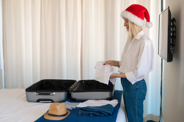 Young woman in a Santa Claus hat in a white shirt and blue jeans collects a suitcase with things on...