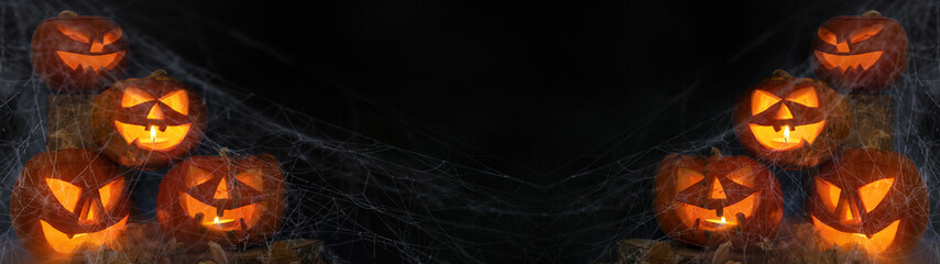 Scary Halloween jack o lantern celebration holiday background banner panorama - Spooky carved pumpkins and dust in the dark black night © Corri Seizinger