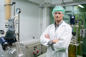 Portrait of chemical scientist male arms crossed and standing in front rotational vaporizer machine for CBD oil extraction at cannabis farm laboratory