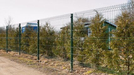a fence made of 3d mesh, in the photo a fence against a background of green trees and gray sky