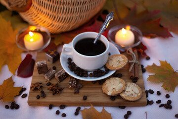 Evening picnic with cup coffee with cookies and chocolate on background of burning candles in autumn park with maple leaves. Still life outdoors