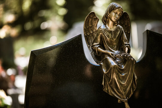 trauriger Engel aus Metall sitzt auf einem Grab