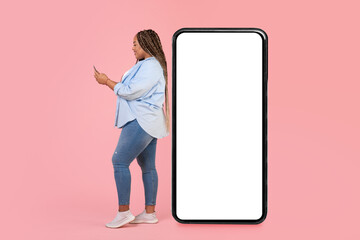 Black Female Using Phone Standing Near Large Smartphone, Pink Background
