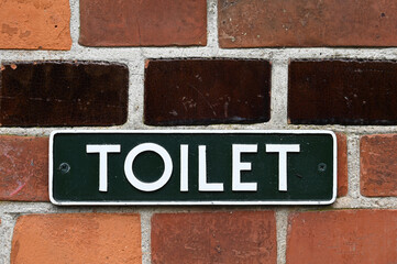 Hinweisschild auf eine öffentliche Toilette an einer Ziegelwand in Dänemark