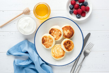 Cottage cheese fritters, Syrniki served with berries, honey and sour cream. Top view, light grey concrete background