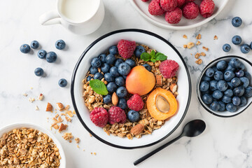 Fruit and berry granola bowl on white marble background. Delicious healthy vegetarian breakfast bowl