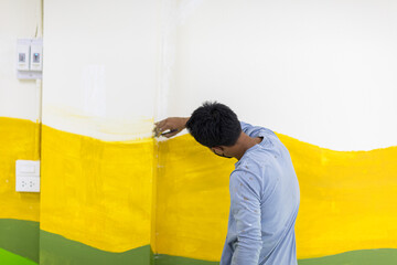 An Asian worker is using a brush to paint a sign outside a building.