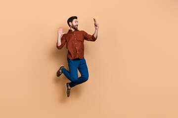 Fototapeta na wymiar Full length portrait of handsome guy jumping arm palm waving hi communicate video chat isolated on beige color background