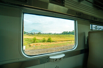 Riding a train in Indonesia sitting by the window watching the tracks and the view outside the window of the train speeding towards its destination