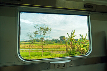 Riding a train in Indonesia sitting by the window watching the tracks and the view outside the window of the train speeding towards its destination