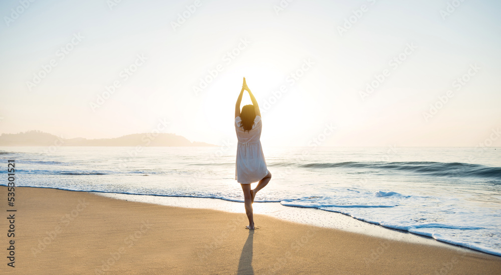 Wall mural Young woman practicing yoga tree position on the beach. - Wall murals