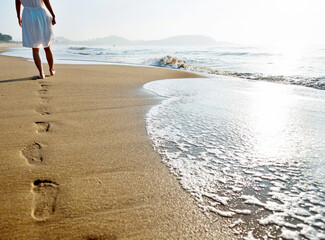 Woman walking on beach leaving footprints in the sand.